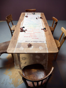 Installation Art: lace colorfully embroidered with a pregnancy poem laid on top of a rustic farm table with accents of hand blown glass filled with sand.